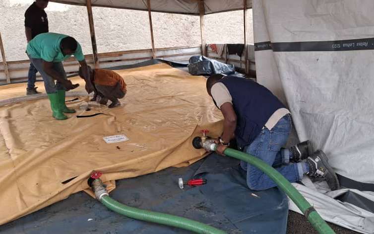  People attach water hoses to a water storage bladder, when filled it will provide water for people in eastern Congo displaced by conflict in the area. 