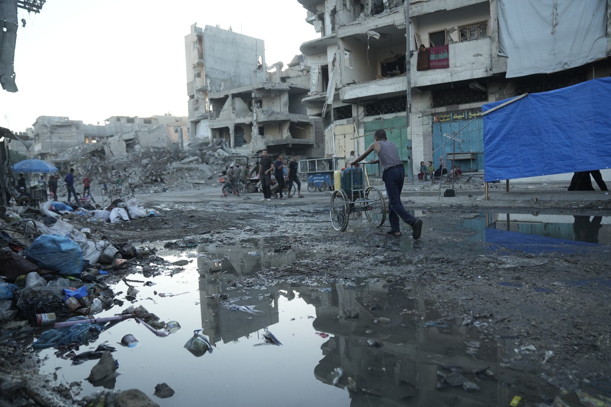 A man pushes a cart loaded with water containers past raw sewage in the street in Gaza City.
